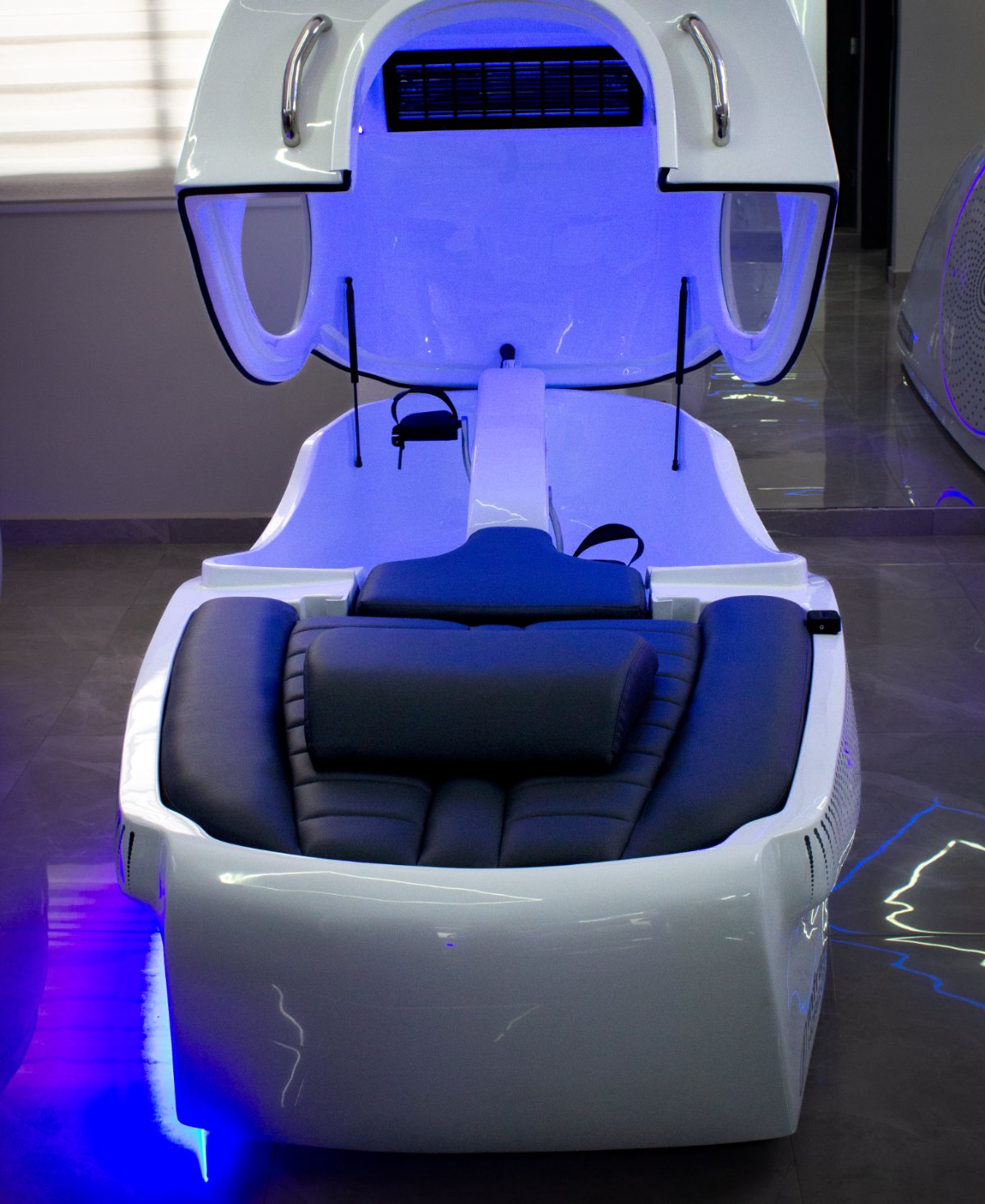 Cabine individual fechada, com iluminação azul e assento reclinado.