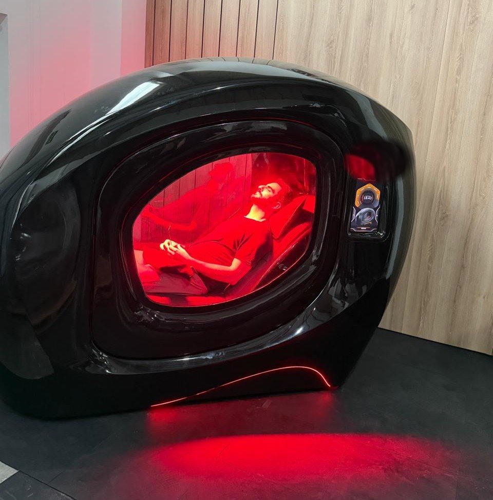 Cápsula fechada de recuperação, com iluminação vermelha e uma pessoa em sessão.